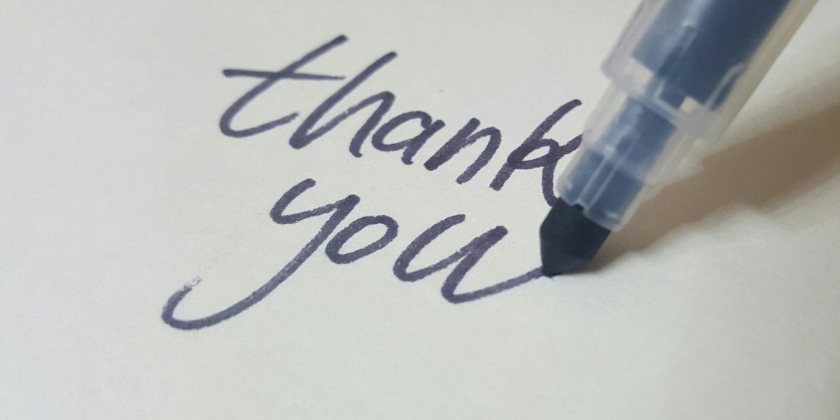 Close-up of a pen writing the words "thank you" on white paper.