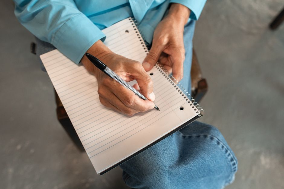 A close-up shot of a person's hands as they thoughtfully write notes with a pen in a notebook on a clean, minimalist surface.