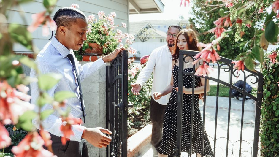 A couple stands in front of a house for sale with worried and uncertain expressions, highlighting the stress and doubt involved in making a poor real estate choice.