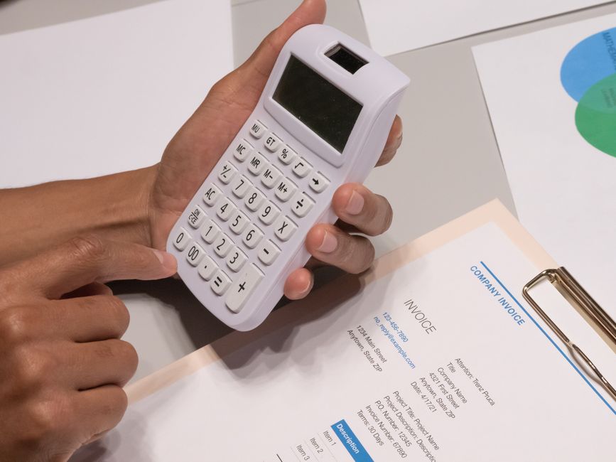Homeowner stands outside their house holding a calculator, thoughtfully weighing the financial pros and cons of selling th...