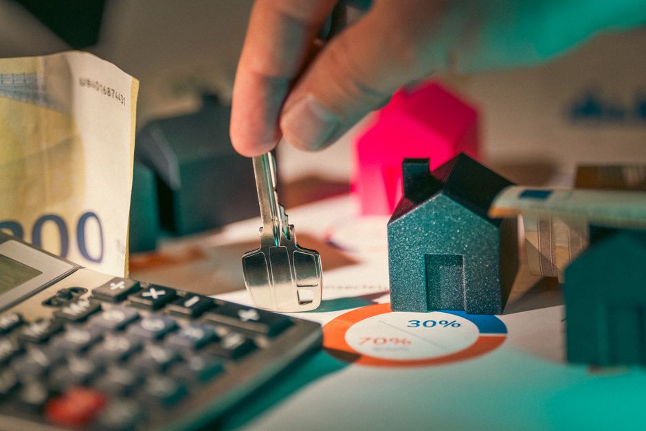 A small model of a house sits next to a piggy bank on a clean surface, symbolizing the theme of saving money on real estate commissions.