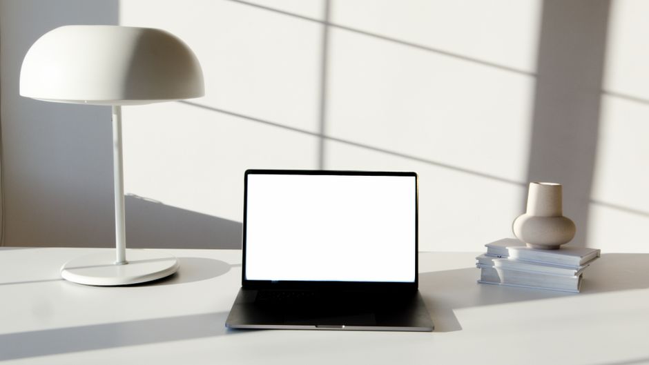 A bright and minimal modern office desk with a laptop, a small architectural model of a house, and a plant, representing a professional and tech-savvy realtor's workspace.