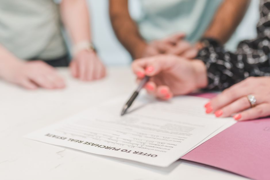 A happy couple signs the final closing documents for their home sale, guided by their real estate agent in a professional and clean office setting.