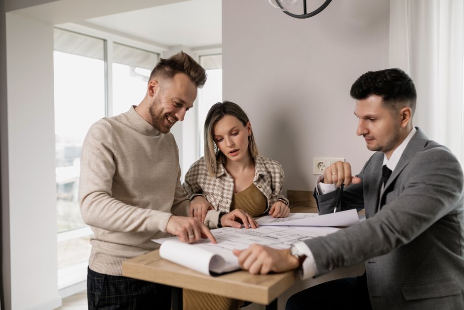 Professional real estate agent sits with a smiling couple at a modern table, transparently explaining the details of a doc... Professional real estate agent sits with a smiling couple at a modern table, transparently explaining the details of a doc...